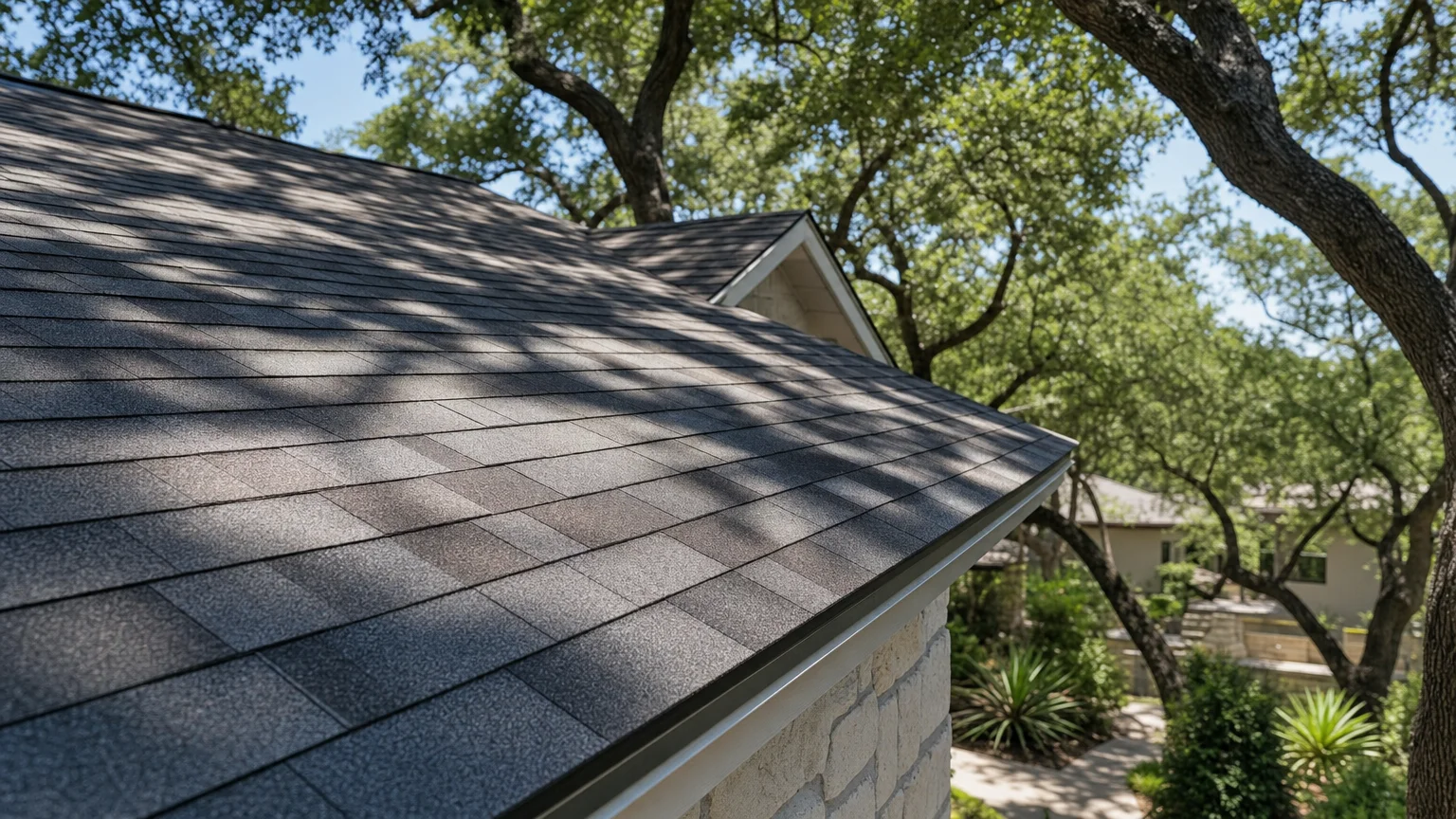 A residential roof in Austin, Texas showing asphalt shingles under bright summer sun with mature oak trees in the background.