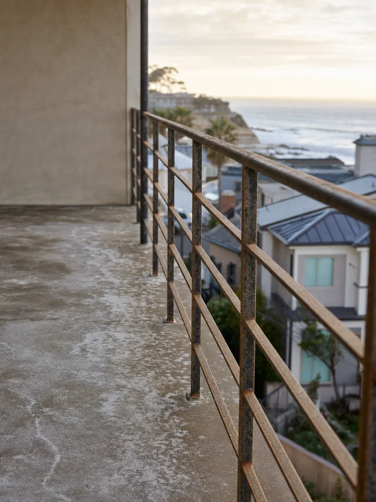 A balcony on a San Diego coastal condo with salt residue staining on the concrete floor and metal railing.